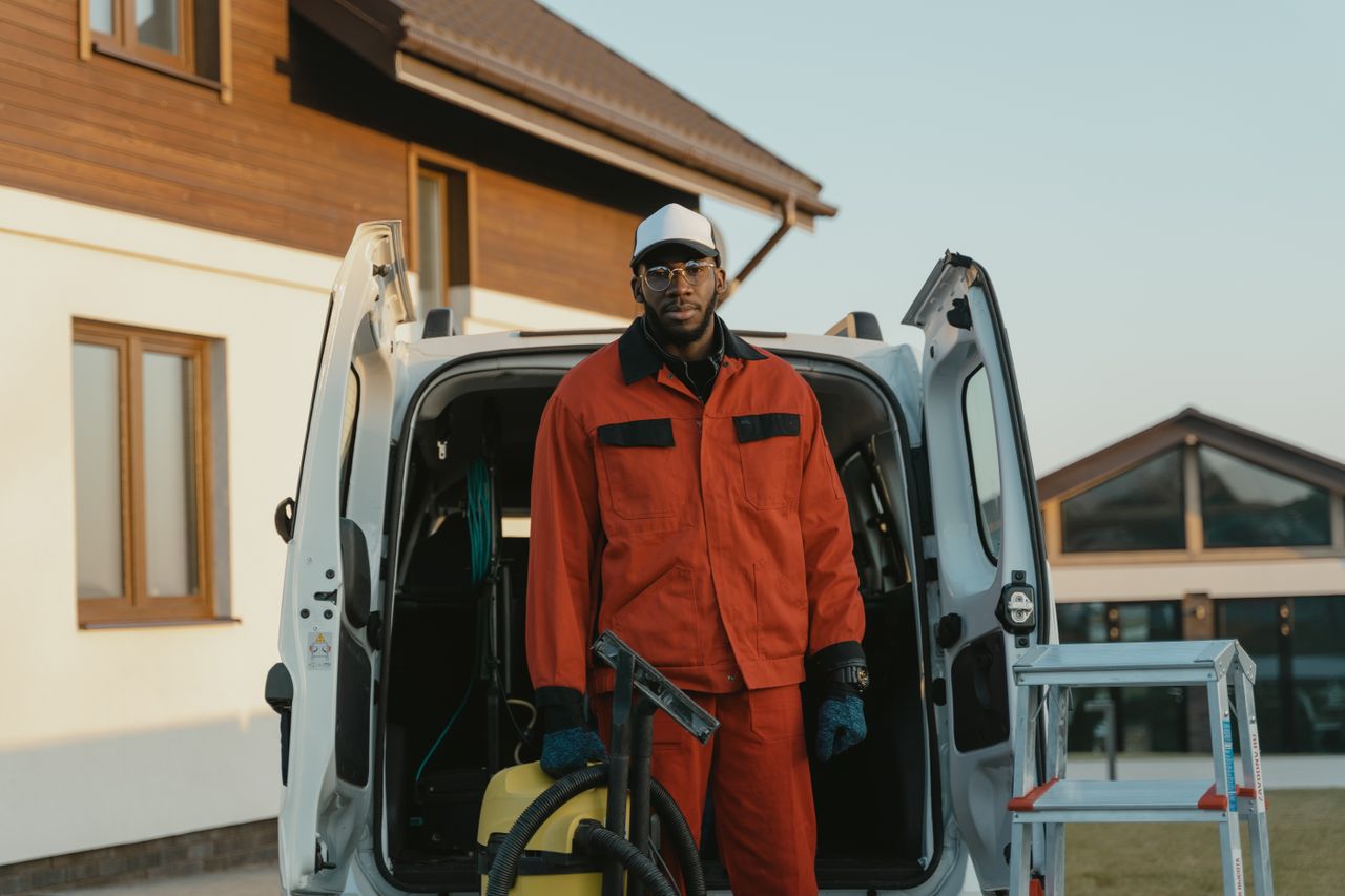 A local service business owner in work clothes beside their van at a residential job site.