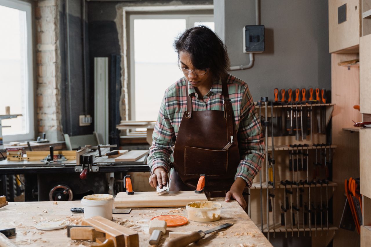 A maker hand-crafting a wood project at a workbench in a bright workshop.