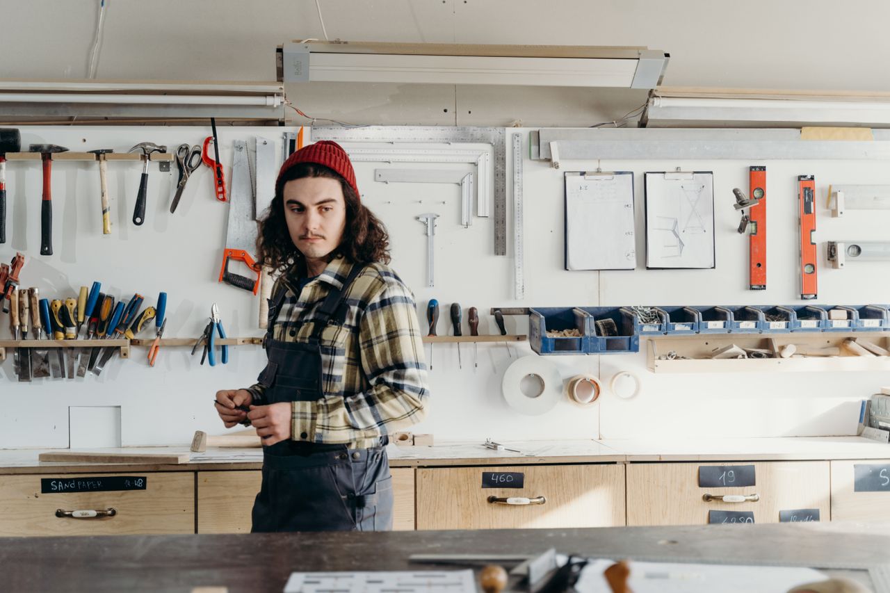 A tradesperson standing with tools in a bright workshop.